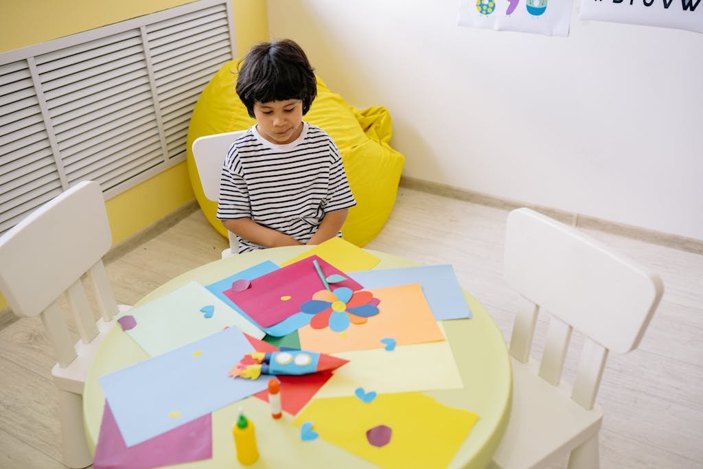 Boy In Striped Shirt Sitting By A Table With Art Materials